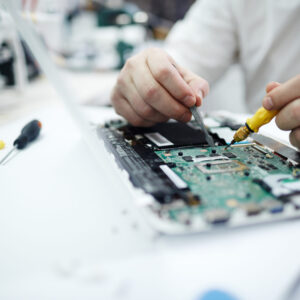 Closeup shot of unrecognizable man fixing circuit board in laptop using screwdriver and different tools on table in workshop