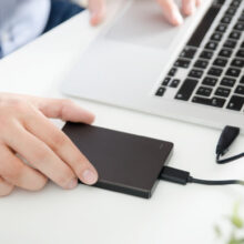 External backup disk hard drive connected to laptop. Man with notebook making safety personal data copy.